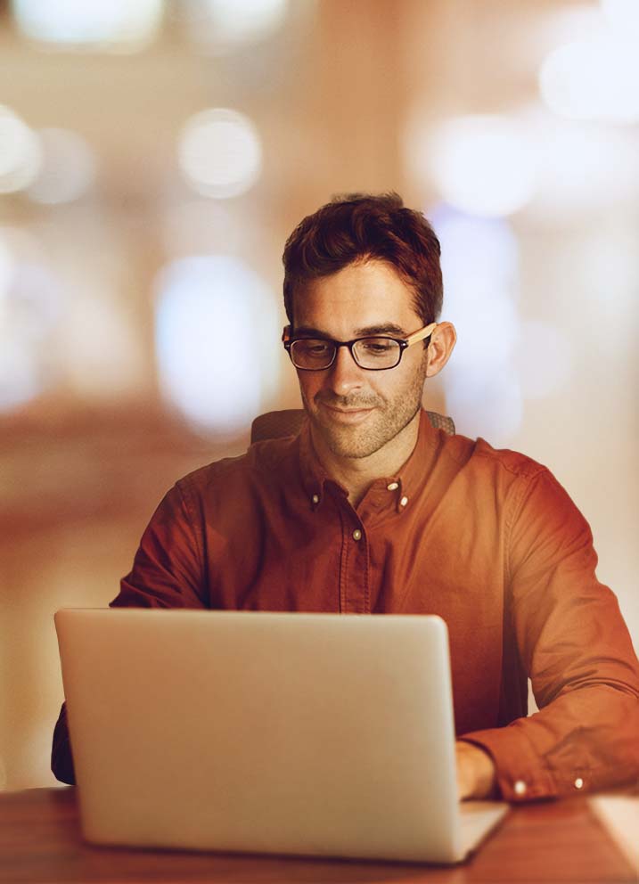 Man in dress-shirt working on laptop, bokeh background