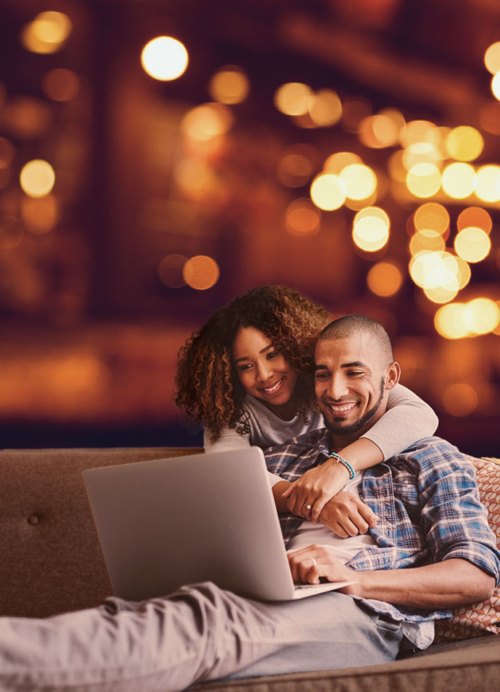 Man and woman using laptop on couch, bokeh background